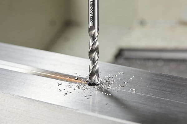 A close-up of a coated carbide drill bit drilling into a hardened steel plate.